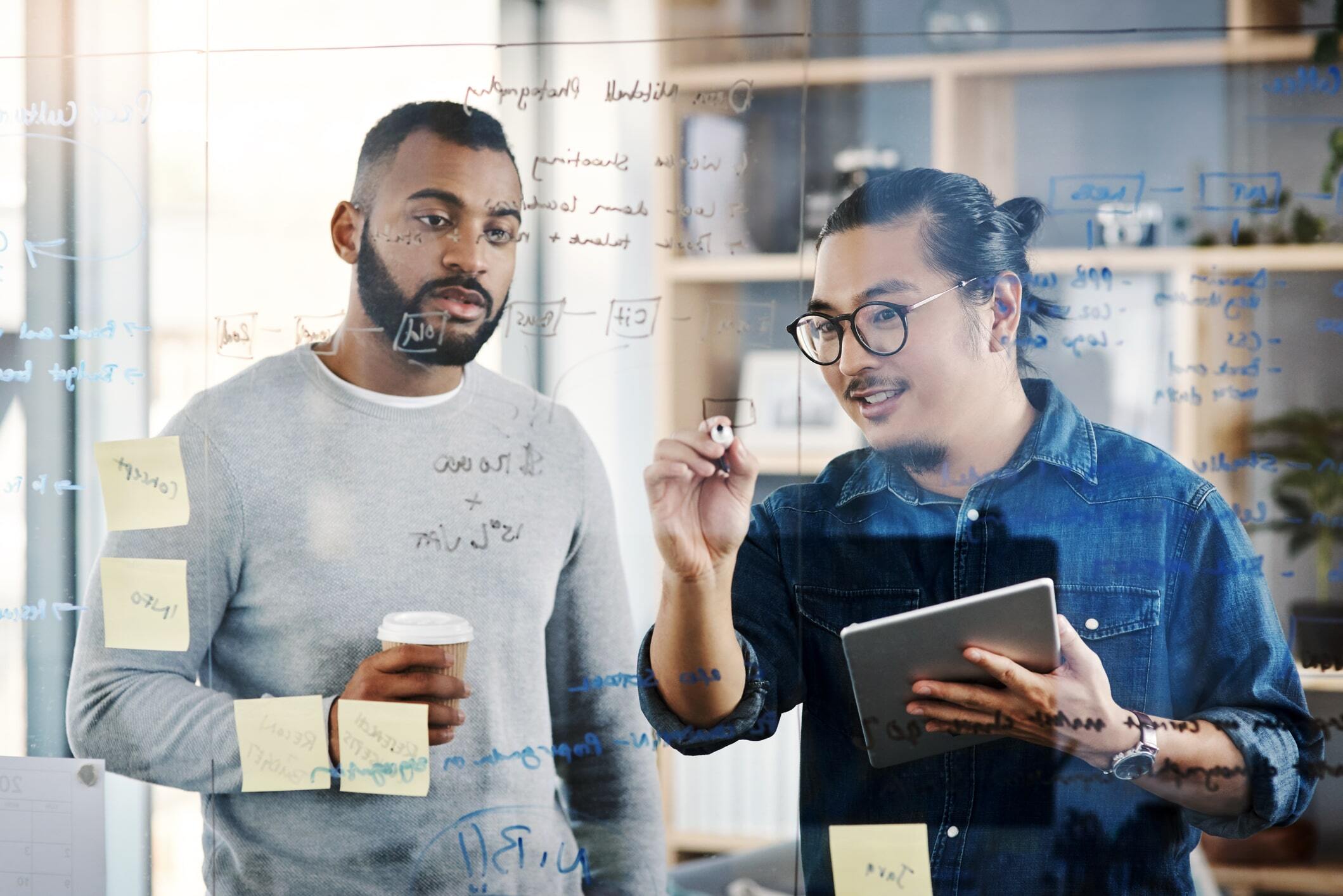 two men discussing project in conference room writing on glass 